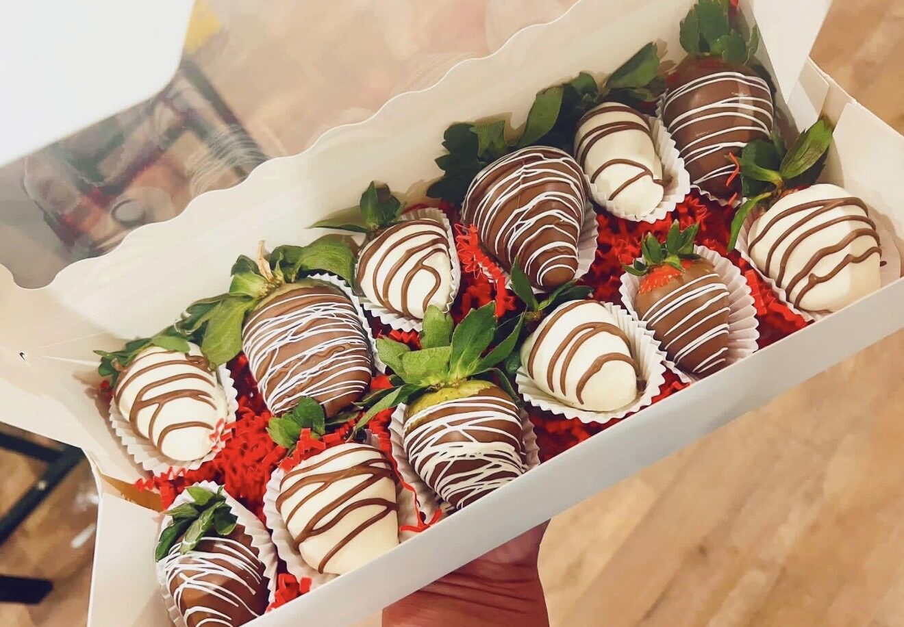 White box of milk- and white-chocolate-covered strawberries drizzled and set on red crinkle paper