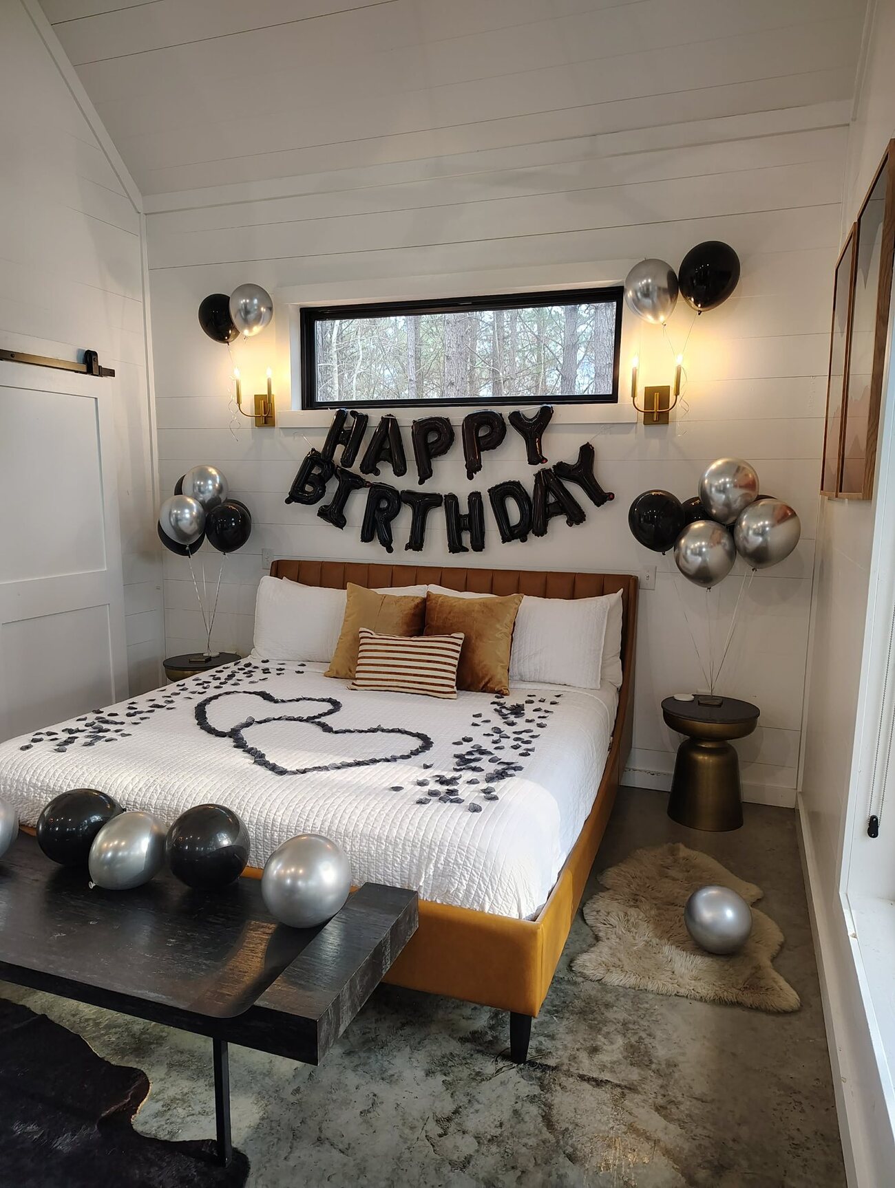 Black Happy Birthday balloon banner and rose-petal double heart on a king bed at The Vine