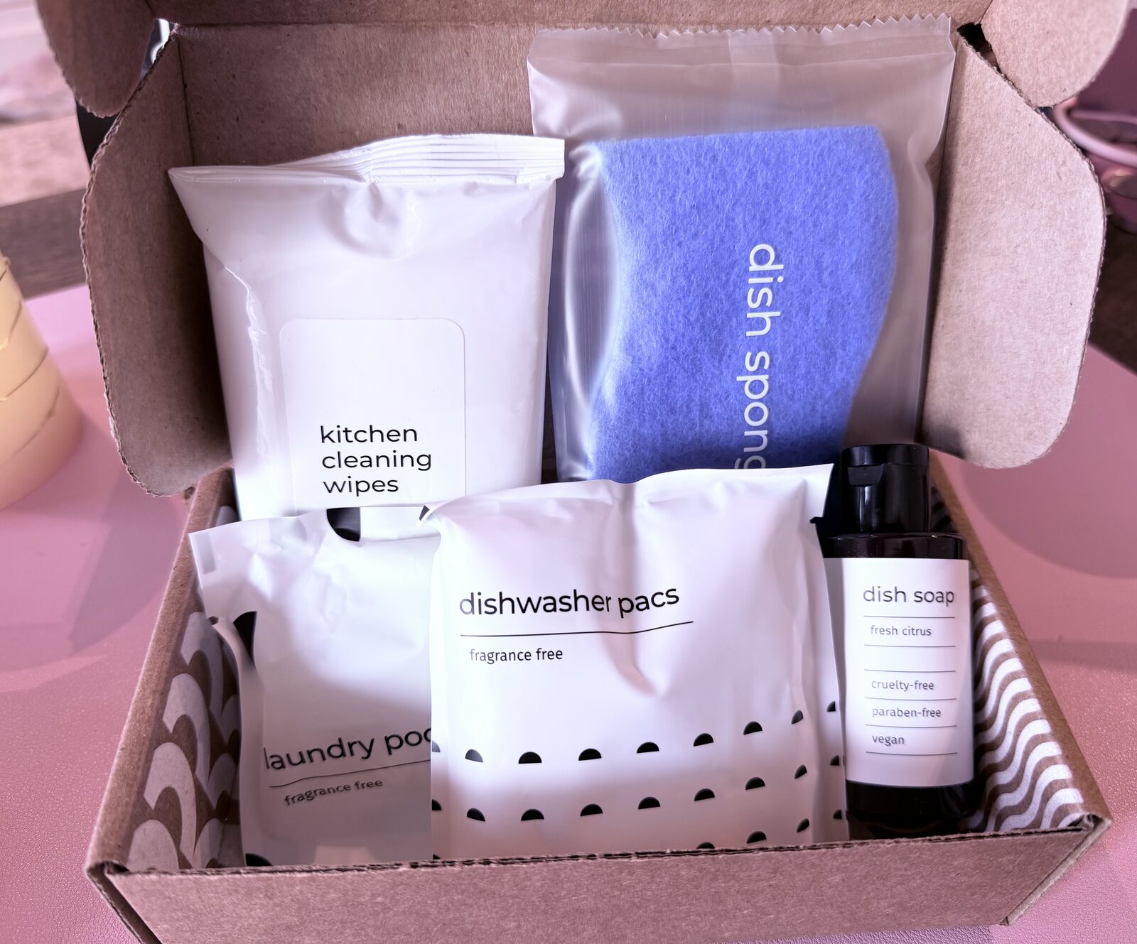 An open kitchen bundle box holding kitchen cleaning wipes, a dish sponge, laundry pods, dishwasher pacs and dish soap