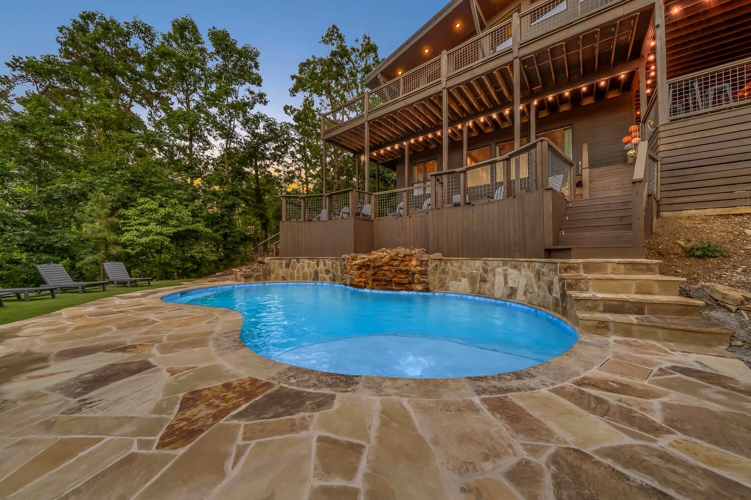 Flagstone pool deck and blue pool below a lit cabin balcony at a client property