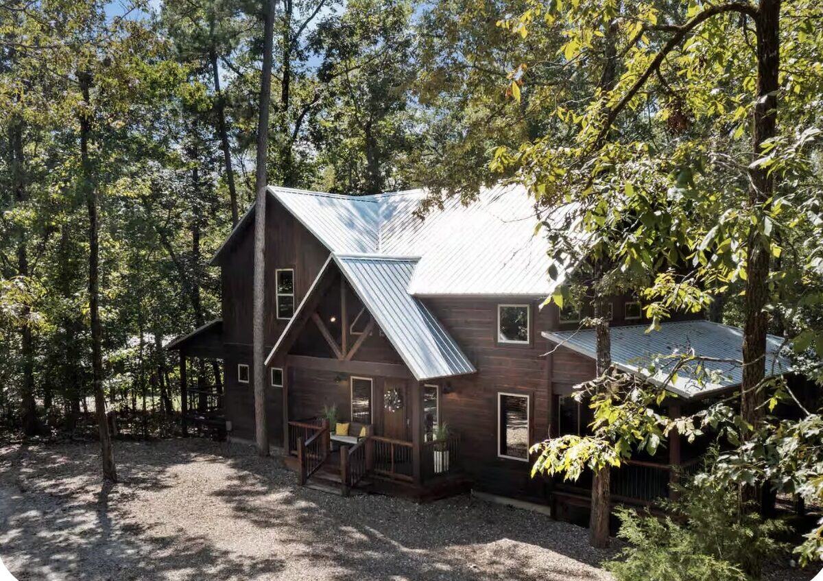 Turn the Page — a dark two-story wood cabin with a metal roof among green woods