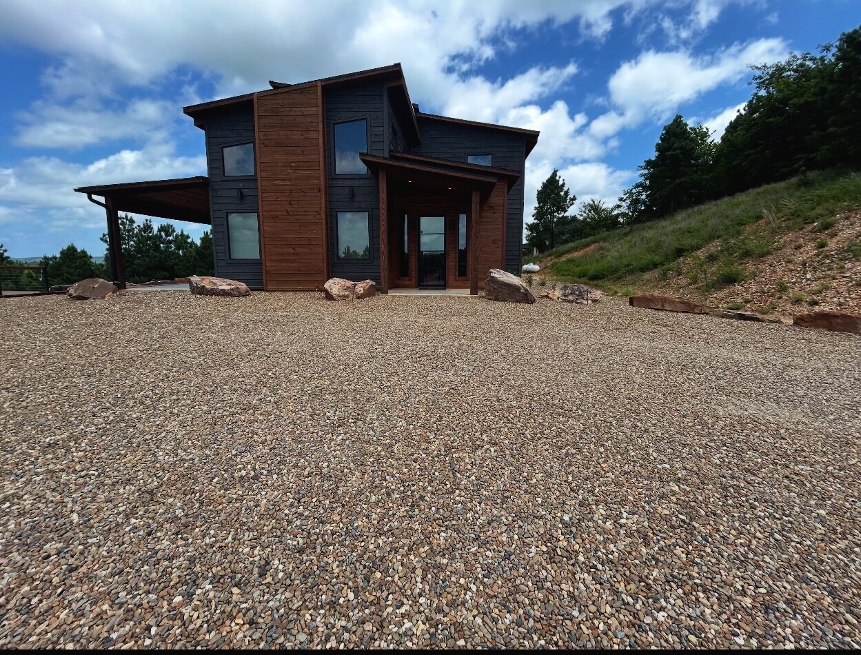 A modern black cabin with a clean, weed-free gravel drive and set landscaping stone