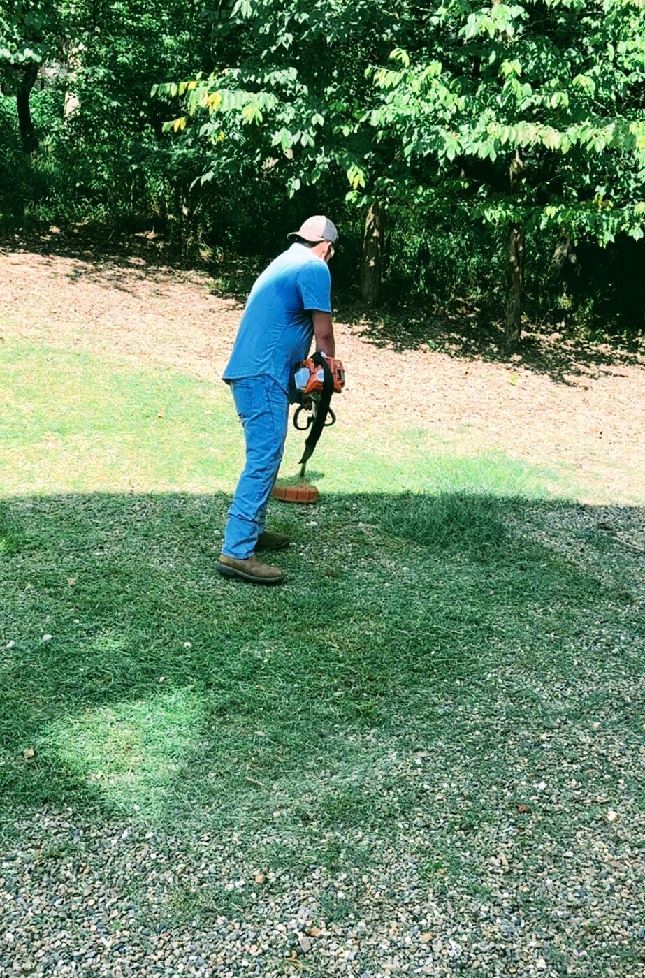 Hochatown Premier crew member using a handheld blower to clear grass clippings off a lawn edge at a cabin