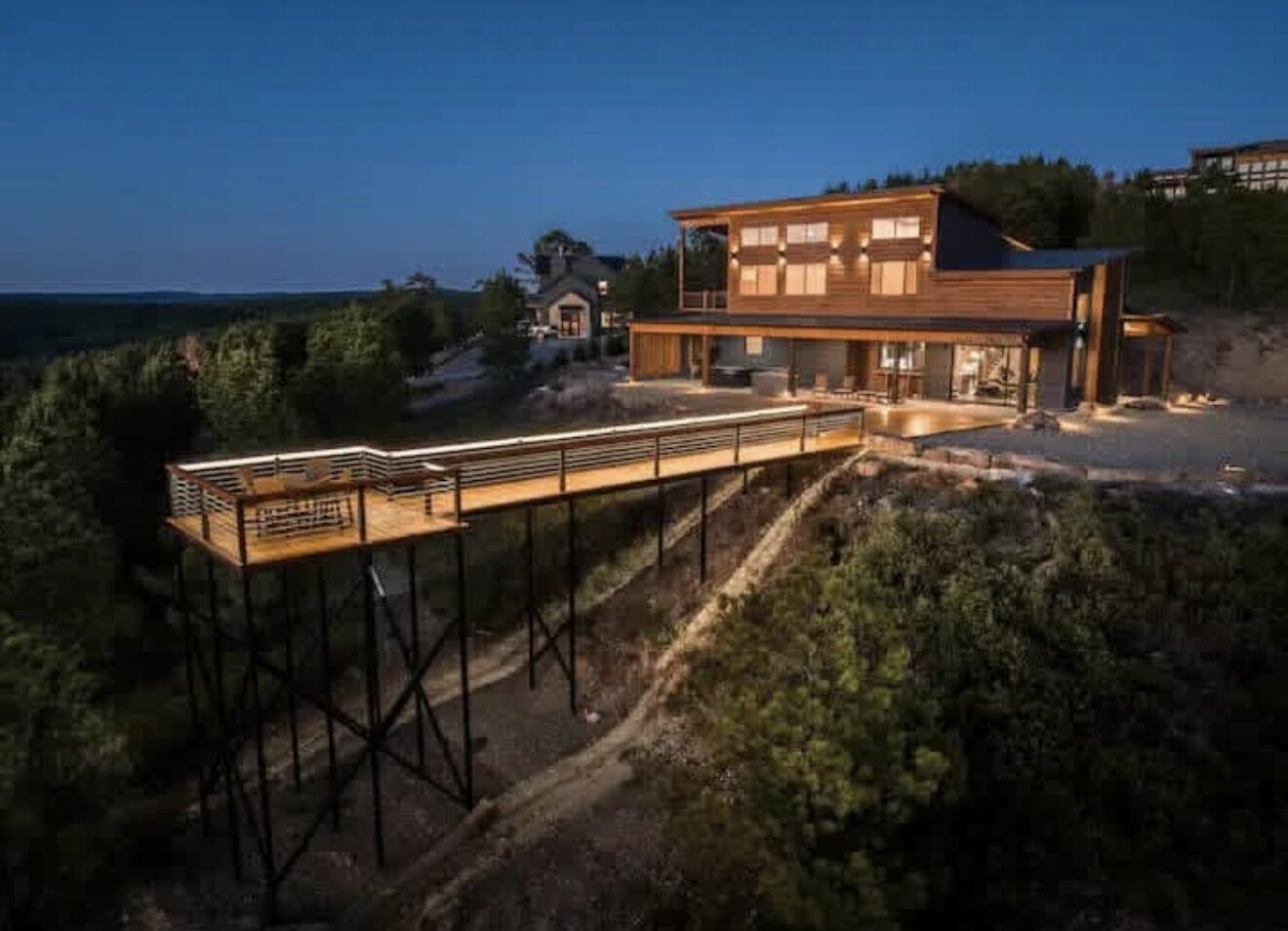 Modern two-story cabin lit at dusk with a long lit catwalk on steel stilts reaching out over the canyon at Sky Deck