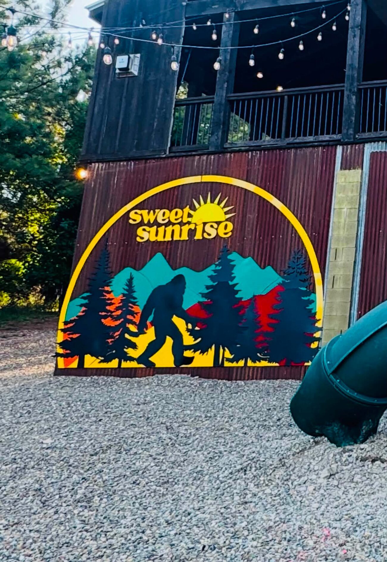 Retro Sweet Sunrise bigfoot mural on the cabin base beside a green tube slide
