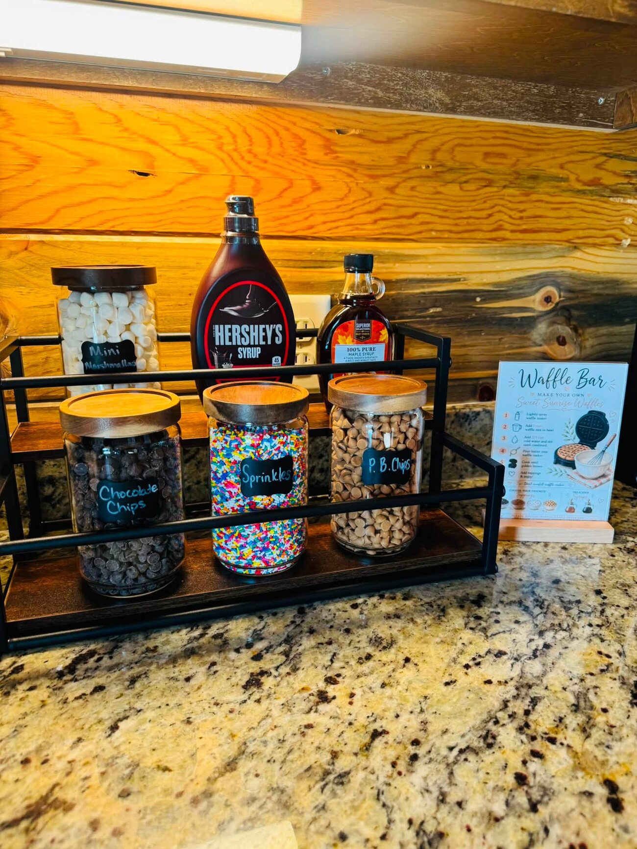 Labeled topping jars — sprinkles, chocolate chips, PB chips — in a black rack with a Waffle Bar card